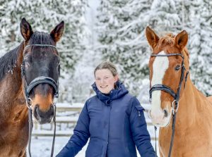 Smiling equestrian with two horses in snow, showcasing Cavallo hoof boots and equine gear, winter horse care essentials.