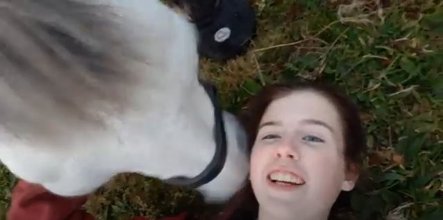 A woman joyfully lies beside a horse wearing Cavallo hoof boots, showcasing equine comfort and care.