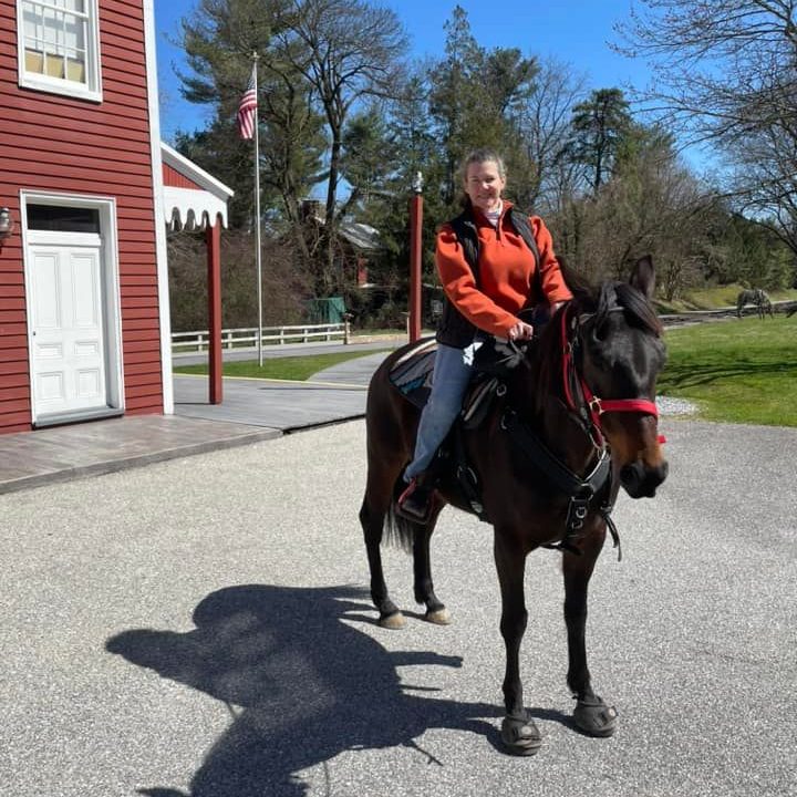 Rider on a horse wearing Cavallo hoof boots near a red building, showcasing equine care gear.