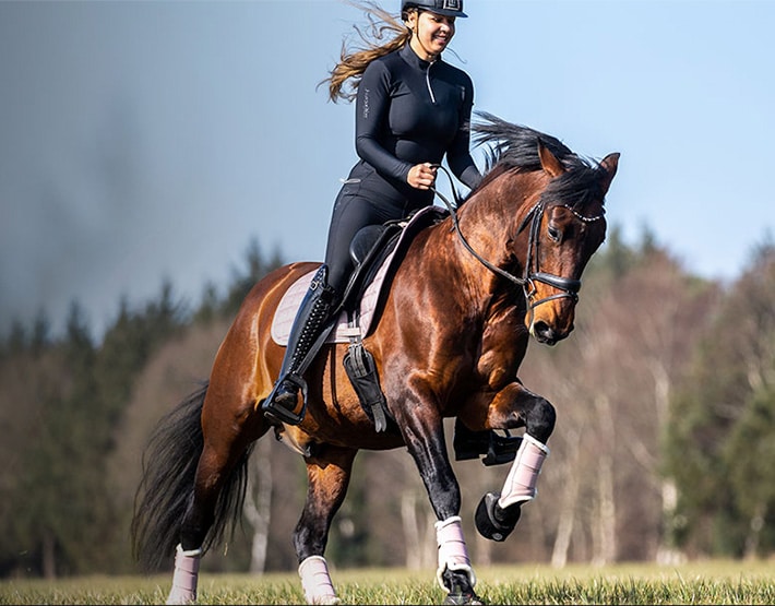 Rider on horse wearing Cavallo hoof boots, showcasing equine gear excellence in a field.