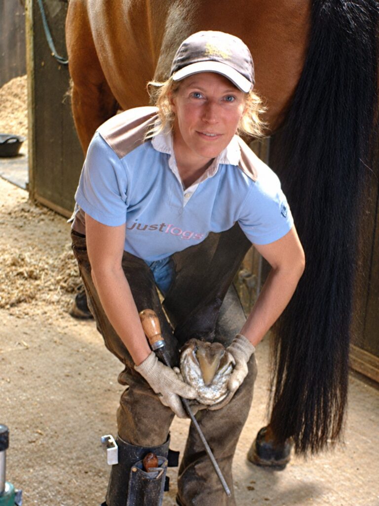 A trimmer in a blue shirt holding up a horse's hoof
